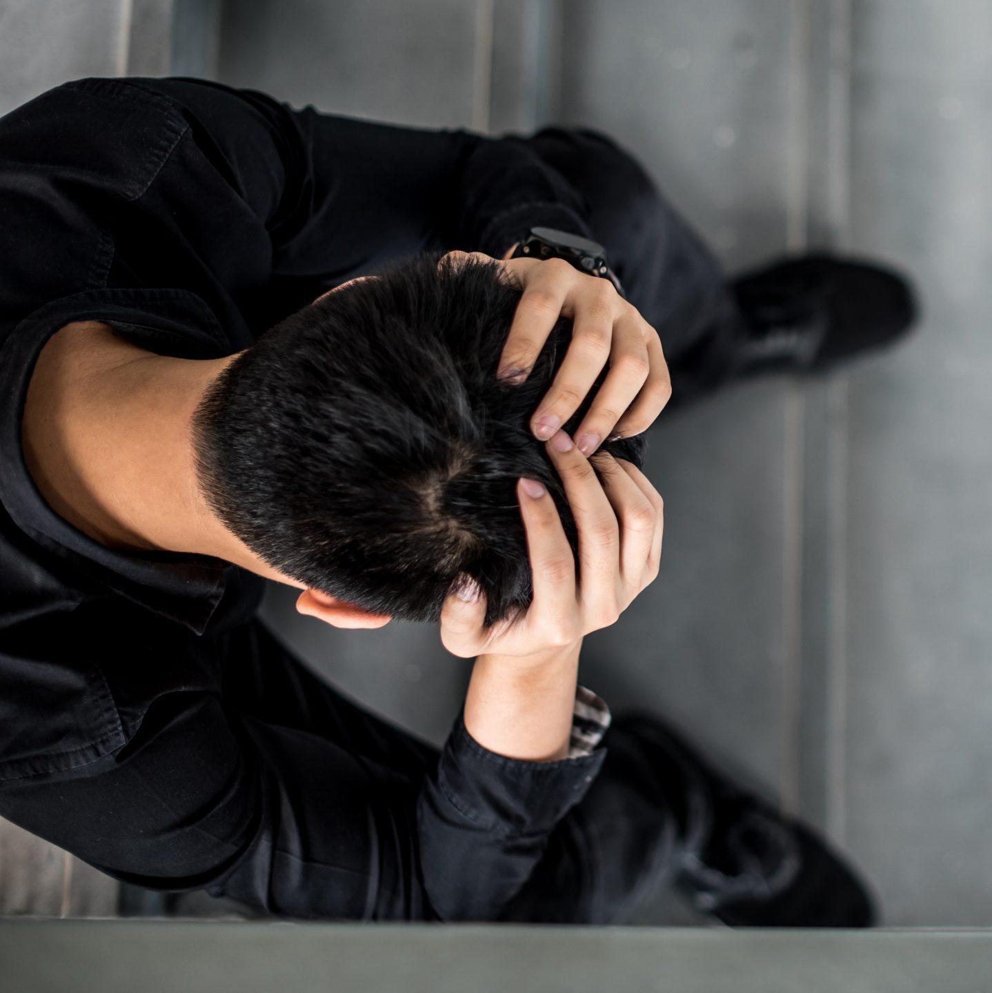 Man sitting on stairs, with his hands on his head, feeling stress and anxiety